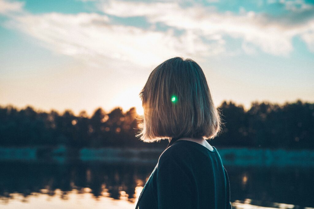 Vrouw die naar de ondergaande zon kijkt, je kan haar gezicht niet zien.