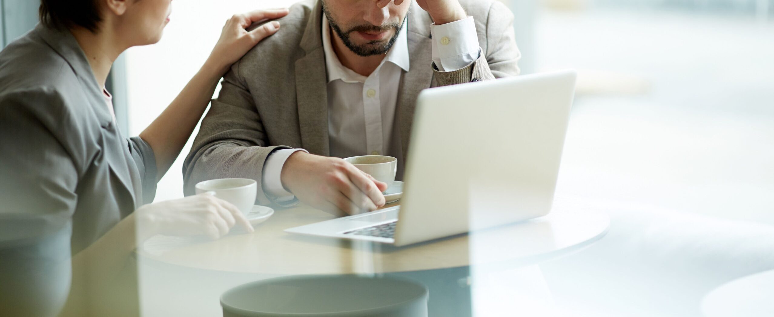 Een man onherkenbaar in beeld. Hij zit achter de laptop. Een vrouw zit naast hem en legt een hand op zijn schouder.