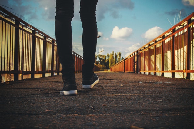 Iemand loopt over een brug, je ziet de broek en schoenen