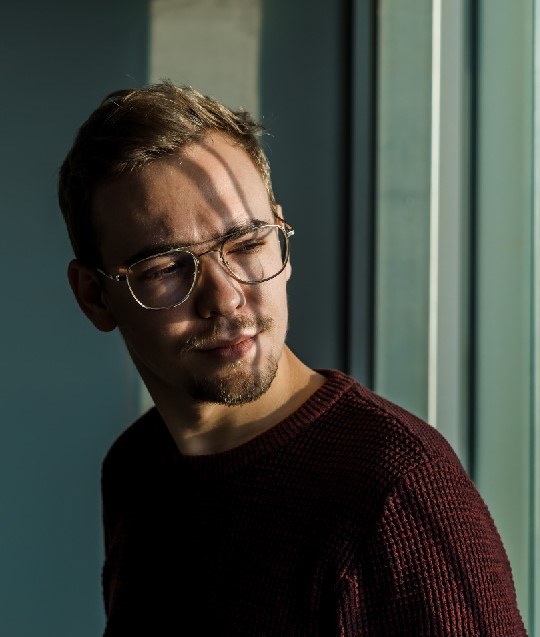 Man met bril en kort blond haar. Hij staat naast het raam, zijn gezicht staat half in de zon en half in de schaduw.